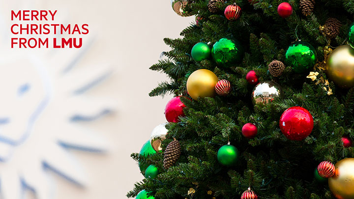 Close up view of a decorated Christmas tree with the LMU spirit mark in the background