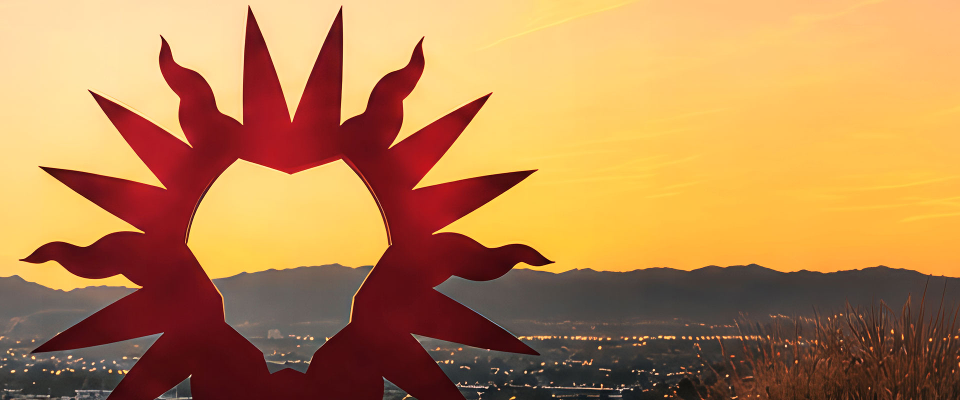 A large LMU Spirit Mark statue at sunset with the opening in the middle of the Spirit Mark facing out across the bluff with Los Angeles in the distance
