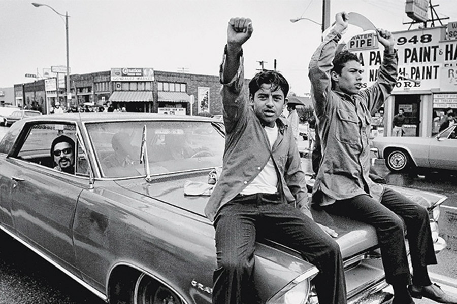 Two men hold up fists in protest on a car hood