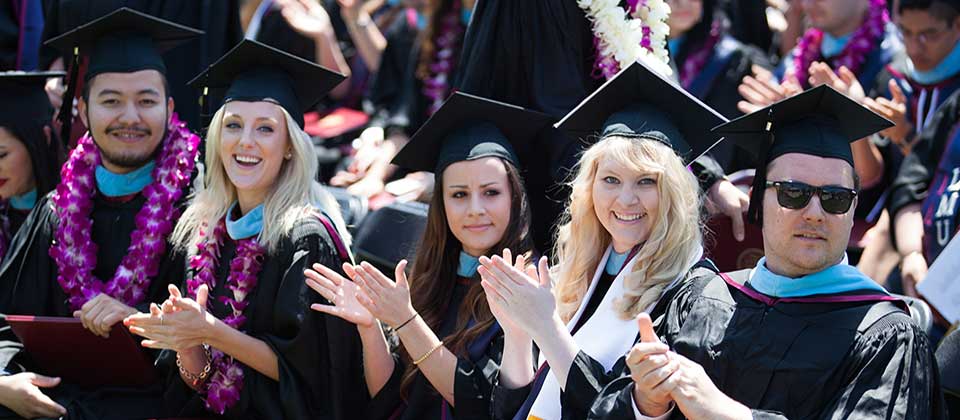 A row of students in their caps and gowns clap and smile at a commencement ceremony.