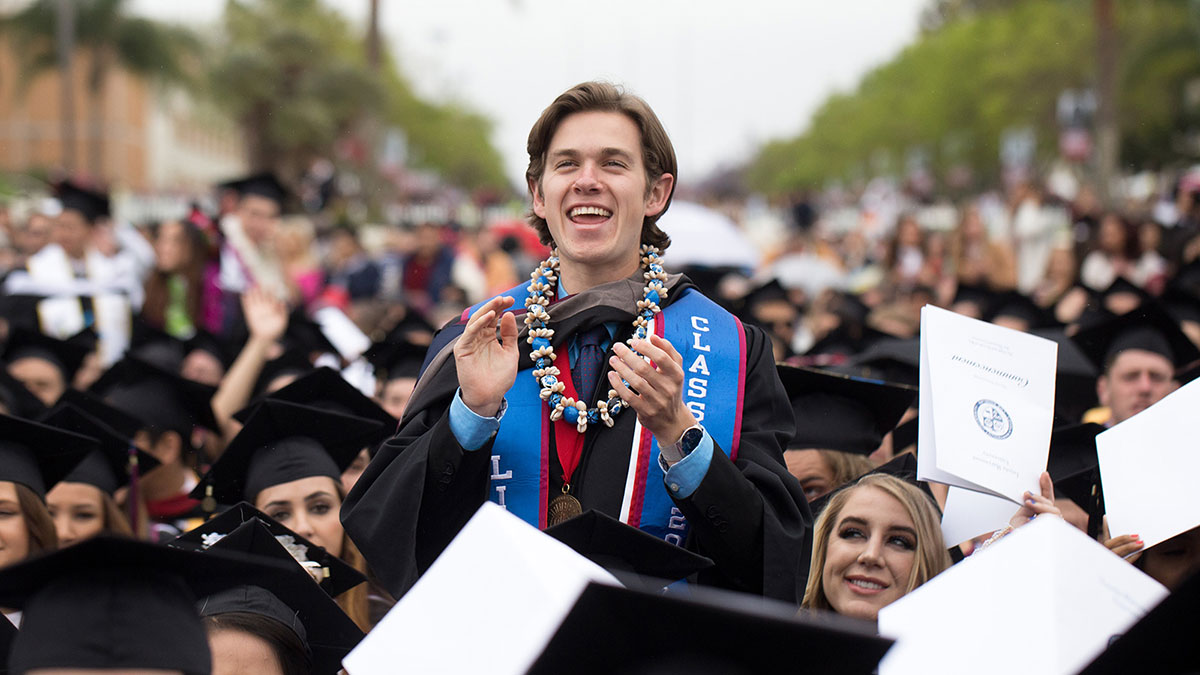 A graduate standing from their seat and clapping during commencement