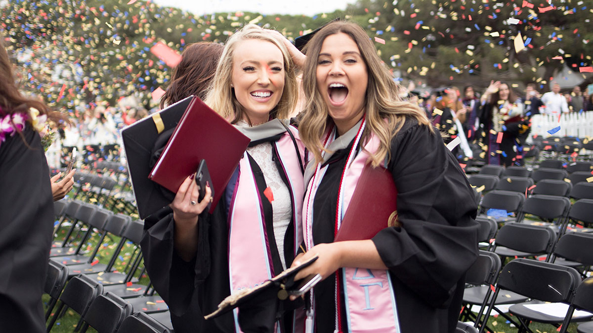 Two newly graduated students excitedly smiling and looking into the camera with confetti in the air around them