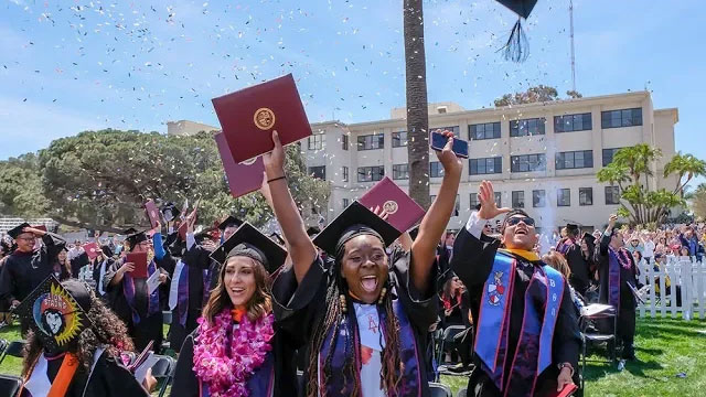 Graduates cheering and celebrating as confetti floats through the air