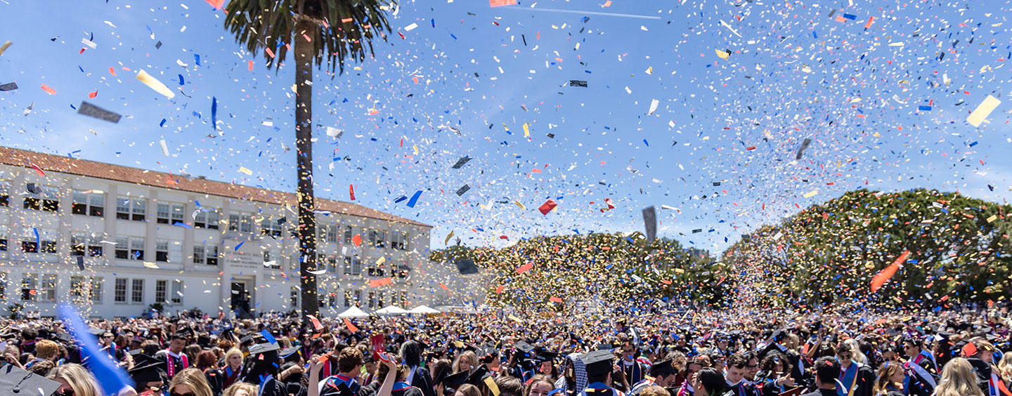 A sea of graduates in sunken garden celebrating and throwing their hats while confetti rains down