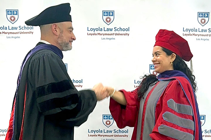 A faculty member shaking the hand of a graduate, both of whom are dressed in graduation attire