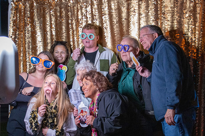 A graduate with various family members posing while wearing and holding up silly props for a photo booth picture