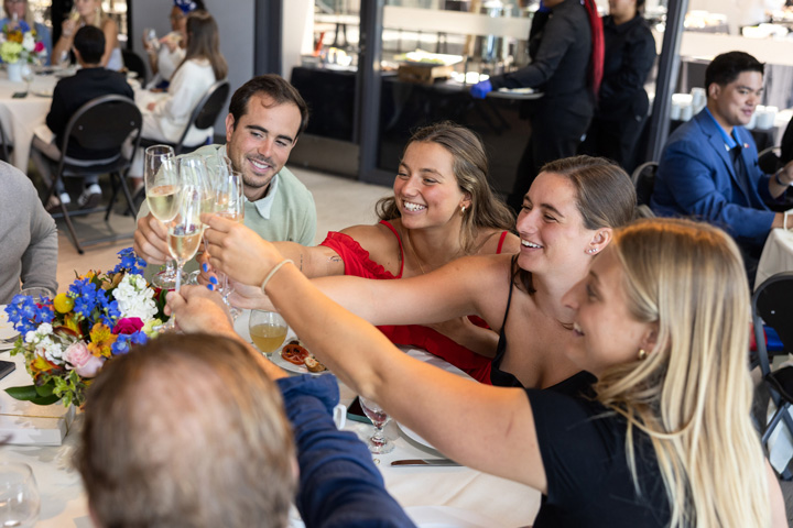 Several graduating students in dress attire toasting while seated at an event