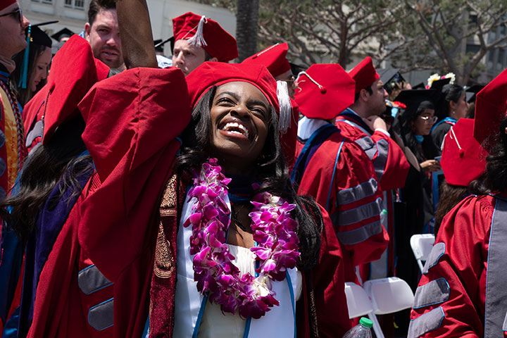 An excited graduate throwing her hand in the air in victory and cheering in excitement during commencement