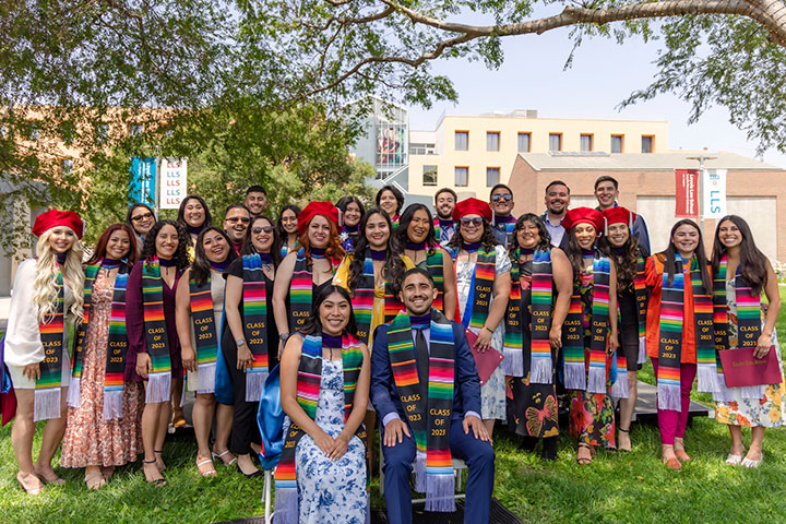 A large group of graduates at the LLS campus smiling and wearing matching sashes